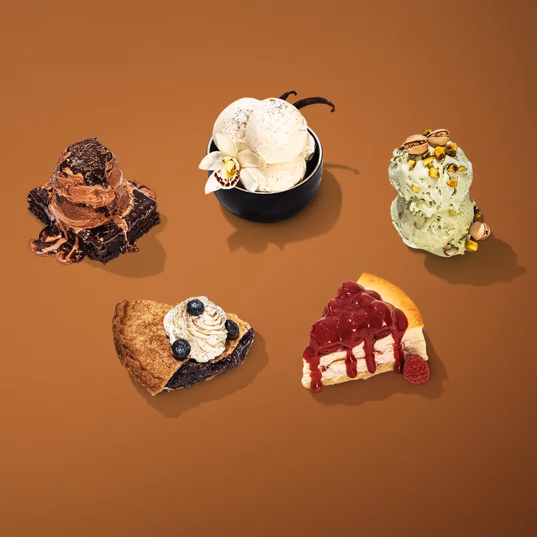 Five desserts on a brown background: chocolate brownie with melting ice cream, vanilla bean ice cream in a black bowl, pistachio ice cream, a berry pie slice with whipped cream, and a cherry-topped cheesecake slice.