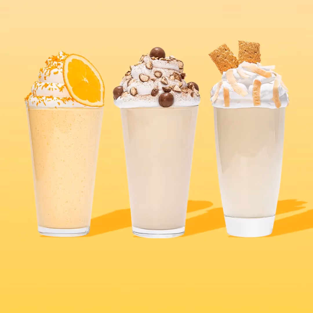 Two glasses of drinks with whipped cream. Gingerbread man and sprinkles on one, candy cane and flecks on the other. Wrapped in a red plaid scarf against a red background.