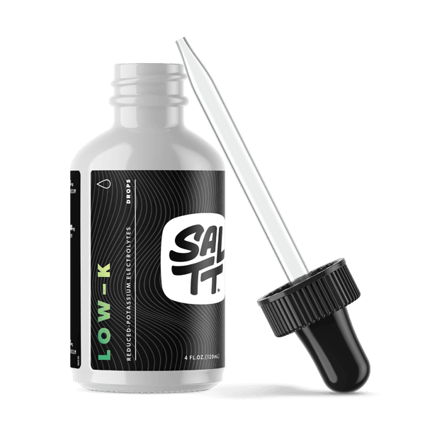 White bottle of SALTT LOW-K Reduced-Potassium Electrolytes Drops. The black label displays the SALTT logo in white, green LOW-K text, and states 4 FL.OZ. (120mL). A separate black and silver dropper is shown next to the bottle.